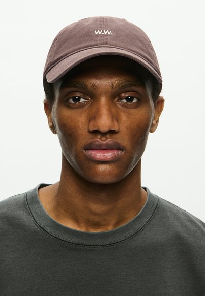 Brun keps med "W.W." broderat i vitt, bärs av en modell. Modellen har på sig en mörkgrå sweatshirt med rund hals. Neutral bakgrund.