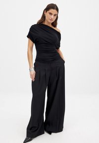 Must mustristi ülaosaga must topp tekstureeritud kangast, millele on lisatud laiad mustad püksid. Täiendav detail: hõbedased käevõrud randmel.