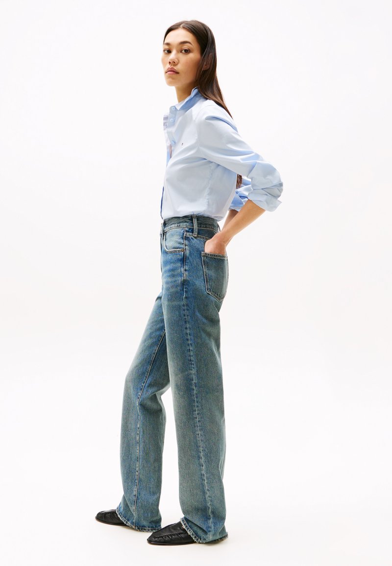 Lichtblauwe overhemden met opgerolde mouwen, gecombineerd met hoge taille, wijde, vervaagde denim jeans en zwarte platte schoenen.