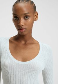 Top in maglia a coste blu chiaro con scollatura ampia a giro e maniche lunghe, caratterizzato da una forma aderente e dettagli testurizzati sottili.