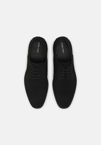 Chaussures Oxford noires en matière lisse et mate, présentant un design classique, un bout arrondi et un laçage minimaliste sur le dessus.