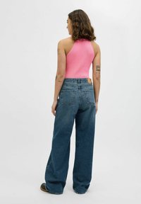 Rožinė įpjovos bodysuit su brūkšninio rašto variantu, derinama su aukšto liemens, laisvai krentančiomis tamsiai mėlynomis džinsomis. Turintis galinius kišenius ir rudą odinį emblemą.