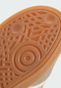 Semelle de chaussure en caoutchouc avec un profil complexe, présentant des cercles et des lignes. La couleur est orange clair avec une texture lisse et des bords définis.