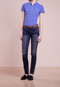 Piké i ljusblå bomull med krage och en liten logotyp; kombinerad med mörkblå denimjeans och svarta loafers. Brunt läderbälte ingår.