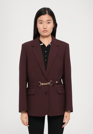 Blazer bordeaux au design ajusté, avec un bouton front unique, deux poches et un détail de ceinture en chaîne dorée à la taille.