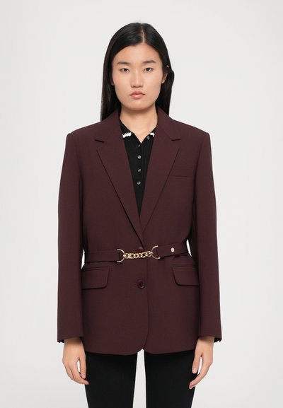 Blazer bordeaux au design ajusté, avec un bouton front unique, deux poches et un détail de ceinture en chaîne dorée à la taille.