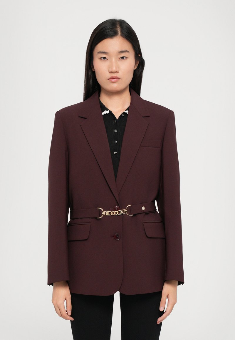 Burgundy blazer with a tailored design, single front button, two pockets, and a gold chain belt detail at the waist.