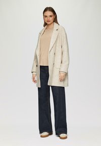 Beige textuur gebreide wolmix jacket met grote revers en dubbele knopen, gedragen over een gestreepte blouse, gecombineerd met donkere wijde jeans.