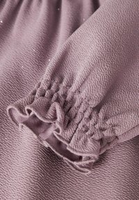 Tessuto viola con una trama ondulata, caratterizzato da polsini elasticizzati arricciati con bordi frills, e sottili scintillii sparsi.