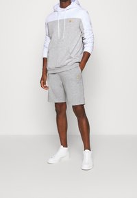 Felpa grigia con parte superiore bianca, cordini e logo. Pantaloni corti grigi con accento giallo, abbinati a sneaker bianche.