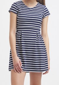 Tummansininen ja valkoinen raidallinen lyhythihainen mekko, jossa on istuva body ja leveä helma. Valmistettu pehmeästä, kevyestä kankaasta, jossa on pyöreä pääntie.