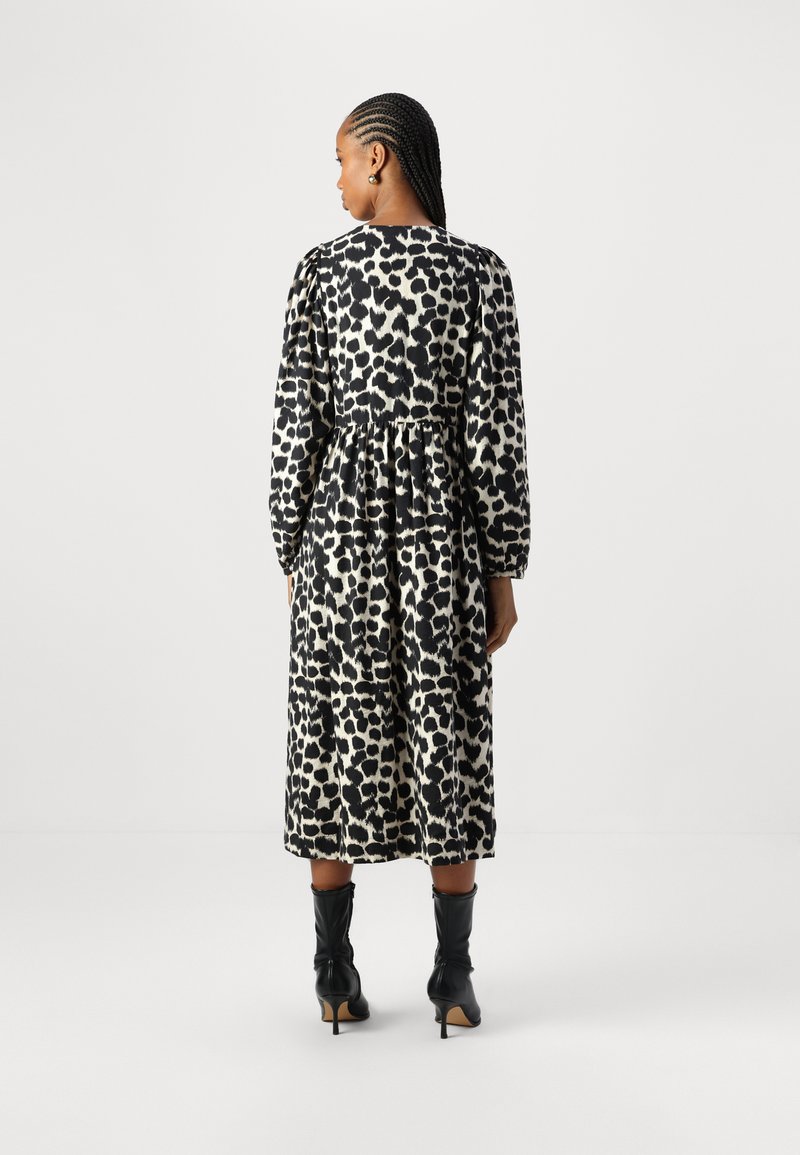 Schwarzes und weißes gepunktetes Kleid mit langen Ärmeln, geraffter Taille und knielangem Saum, kombiniert mit schwarzen High Heels.