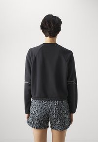 Felpa nera con maniche raglan lunghe, dettagli di cucitura grigia, abbinata a pantaloni corti grigi con un motivo a macchie di leopardo nero.