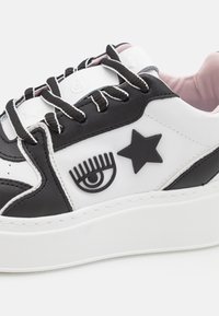 Czarno-białe sneakerki z grubą białą podeszwą. Zawierają wypukłą czarną gwiazdę i grafikę oka. Materiał jest gładki, z czarnymi sznurowadłami.