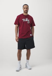 T-shirt Nike marrom com logótipo em branco, combinado com calções pretos. O modelo usa ténis brancos e meias de comprimento normal. Design simples.
