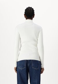T-shirt blanc à manches longues côtelées avec un col montant, associé à un jean en denim bleu à jambes larges avec poches arrière et une coupe légèrement ample.