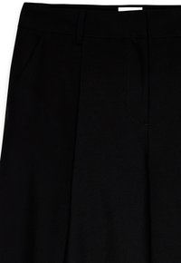 Melnas bikses no gludas auduma, ar plakanu priekšpusi un drēbju krokām, sānu kabatām un jostai paredzētām cilpām jostasvietā.