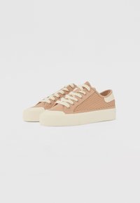 Scarpe sneakers basse color beige con un design testurizzato, lacci crema e una suola in gomma spessa. Presentano una punta liscia e dettagli laterali.