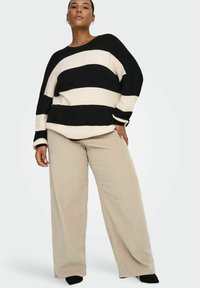 Crni i bijeli prugasti široki pulover sa rebrastom teksturom, uparen s opuštenim bež kordiranim hlačama. Mekani materijal i široki kroj.