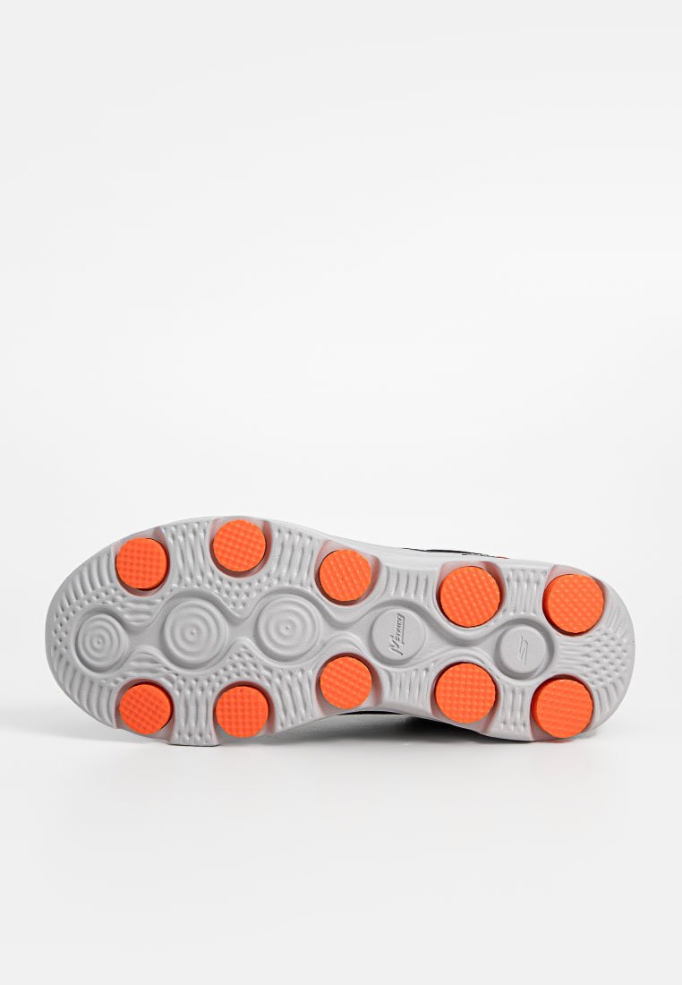 Sole di una scarpa sportiva con base bianca e dieci pad di aderenza circolari arancioni disposti uniformemente su un motivo testurizzato.