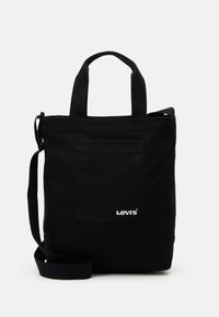 Sac fourre-tout en toile noire avec double poignées, bandoulière réglable, poche externe et logo Levi's blanc sur le devant.