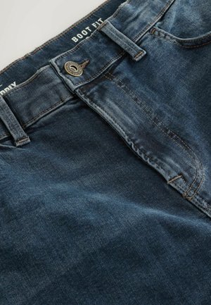 Plave traperice s dizajnom za čizme. Imaju prednje kopčanje na dugme i vidljive šavove. Tekstura je čvrsta s lagano iznošenim izgledom.