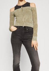 Top corto de canalé verde oliva con diseño de hombros al descubierto, mangas largas y cremallera frontal. Combinado con vaqueros ajustados negros.