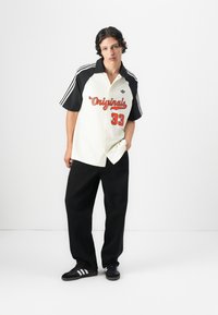 White and black short-sleeve shirt with red lettering and number 33, paired with loose black pants and black sneakers with white stripes.