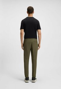Schwarzes kurzärmliges Hemd, kombiniert mit olivgrünen, taillierten Hosen mit elastischem Bund und Reißverschluss Gesäßtasche. Schwarze Sneaker inklusive.