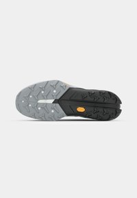 Semelle de chaussure de sport noire et grise avec un profil en caoutchouc agressif, présentant une surface texturée et un logo Vibram proéminent en orange.