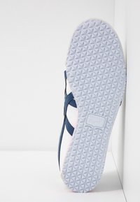 Marineblå och vit sneaker med en texturerad gummisula. Har en slät läderöverdel och en kontrasterande rosa accent nära sulan.