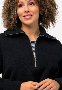 Pullover nero in pile mezza zip con colletto alto, zip dorata e fodera interna a righe. Texture morbida con vestibilità comoda.
