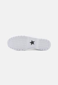 White sneaker sole with textured traction pattern, featuring a black star logo at the midsole, smooth finish, and rounded toe design.