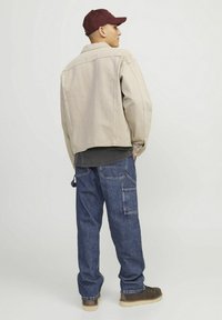 Jachetă din denim bej, blugi cargo albaștri și cizme maronii. Jacheta are o croială lejeră și un guler. Șapca este bordo cu un logo.