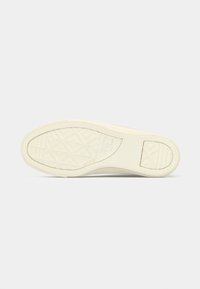Semelle de chaussure en caoutchouc de couleur blanc cassé avec un motif de grip texturé. Présente une forme arrondie et une marque sur le côté embossée dans le matériau.