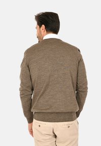 Maglione marrone lavorato a maglia con scollatura rotonda e orlo a costine, caratterizzato da maniche lunghe e una texture morbida, abbinato a pantaloni beige.