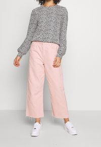 Top a maniche lunghe con motivo floreale in bianco e nero abbinato a pantaloni larga rosa chiaro e sneakers bianche. Tessuto testurizzato, vestibilità rilassata.