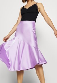 Liliowa satynowa spódnica o rozkloszowanym kroju, z ukośnym szwem i gładką fakturą. Połączona z czarną kamizelką z koronkowym wyko ńczeniem.