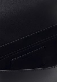 Intérieur d'un sac en cuir noir montrant un doublure texturée et une poche intérieure avec un logo en relief subtil.