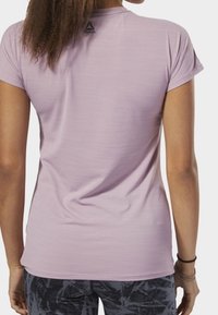Krátký rukáv, fialové sportovní tričko s hladkou texturou a jemným leskem. Má logo na horní části zad a přiléhavý střih.