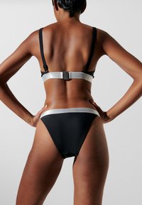 Set di bikini nero con banda accentuata in argento. Il reggiseno ha spalline regolabili e una chiusura sul retro, mentre la parte inferiore presenta un design abbinato.