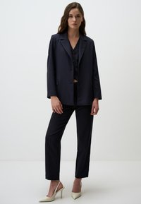 Set di giacca e pantaloni a righe navy, con una vestibilità morbida, rever a punta e chiusura a due bottoni. Abbinato a scarpe con tacco alto color crema.