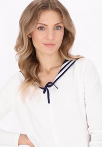 Cardigan bianco con dettagli blu navy al colletto, con un fiocco e chiusura a bottoni. Tessuto morbido, maniche lunghe, design casual.