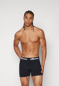 Schwarze Boxershorts aus weichem Stoff, mit einem elastischen Bund, der das weiße "ellesse"-Logo trägt. Figurbetonter Schnitt.