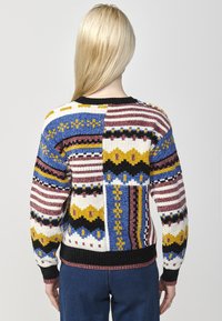 Maglione lavorato a maglia colorato con un motivo patchwork che presenta strisce e pattern geometrici in blu, giallo, rosa e nero. Orlo a coste nero.