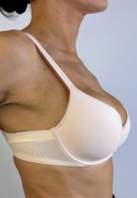 Sostén rosa claro con un diseño liso y acolchado, tirantes ajustables y una banda de malla transpirable en el costado. Presenta detalles de costura sutiles.