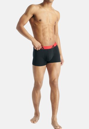 Zwarte boxershorts met een rode elastische tailleband met een logo. De stof is glad en aansluitend, ontworpen voor comfort en ondersteuning.