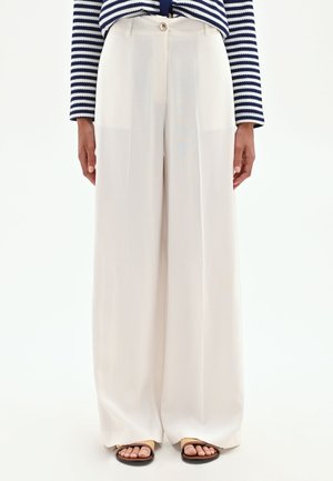 Femme portant un pantalon taille haute à jambes larges couleur écrue, un haut à manches longues rayé bleu marine et blanc, et des sandales ouvertes aux orteils.