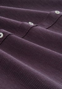 Burgundy fabric with a textured, small-scale grid pattern. Features white buttons and visible stitching on the placket. Smooth finish.