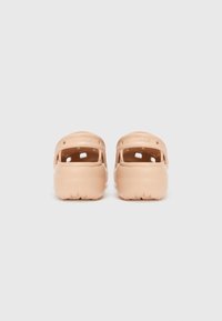 Light peach Crocs with a smooth plastic exterior, ventilated sides, and a back strap for secure fit. Textured sole for grip.